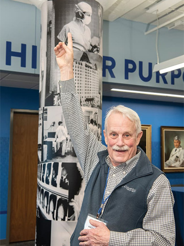 Medical School Alumni pointing at a younger picture of himself during the surgery wall dedication