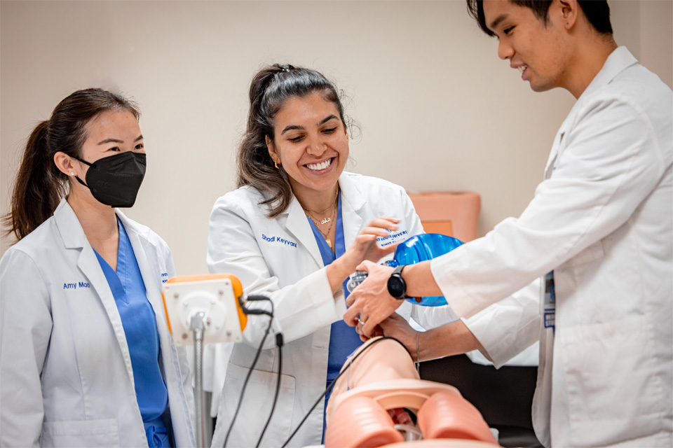 Photo of two or three students at the sim center wokring together to learn new techniques